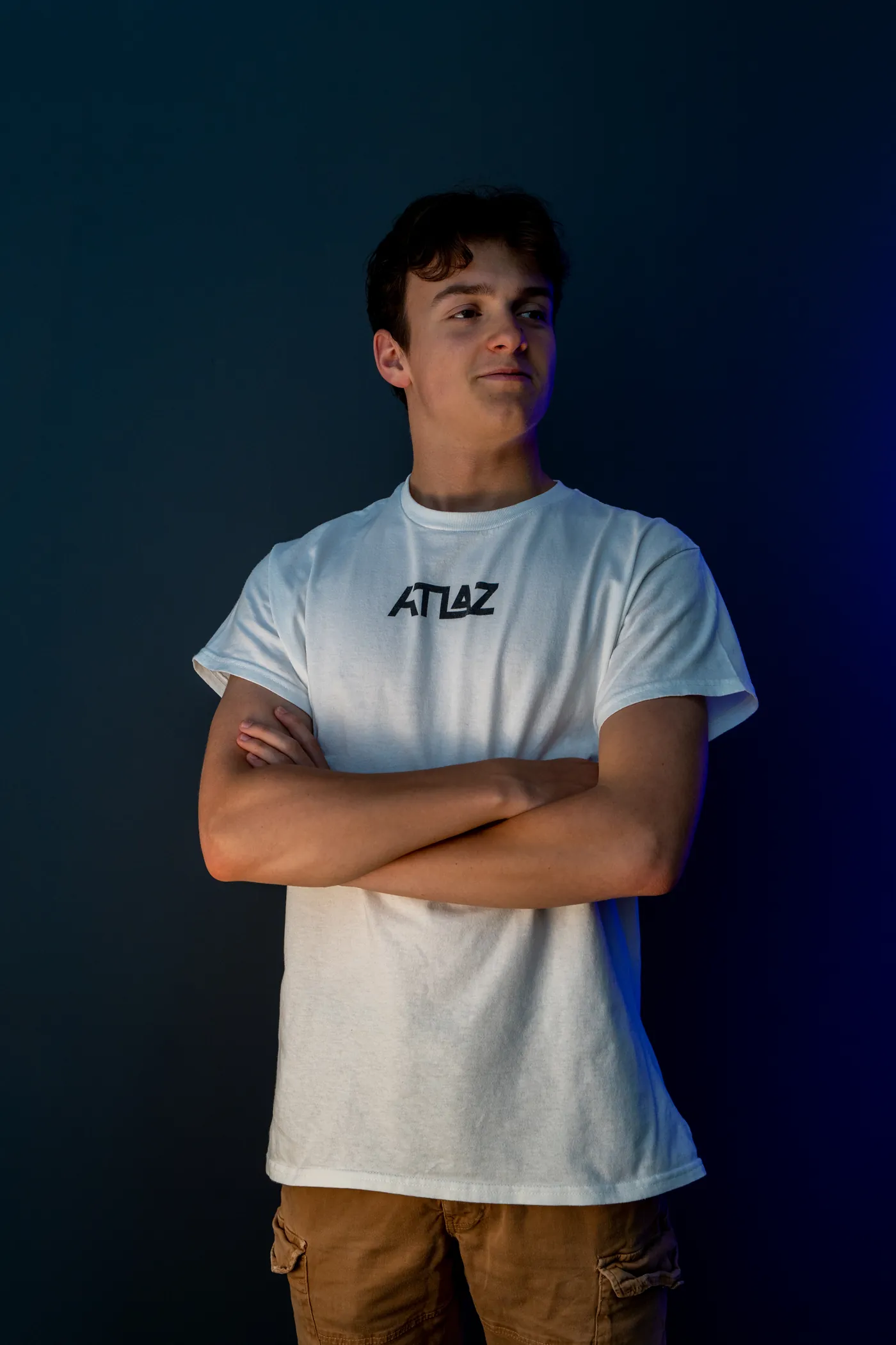 Portrait of ATLAZ in a white ATLAZ shirt against a dark blue wall